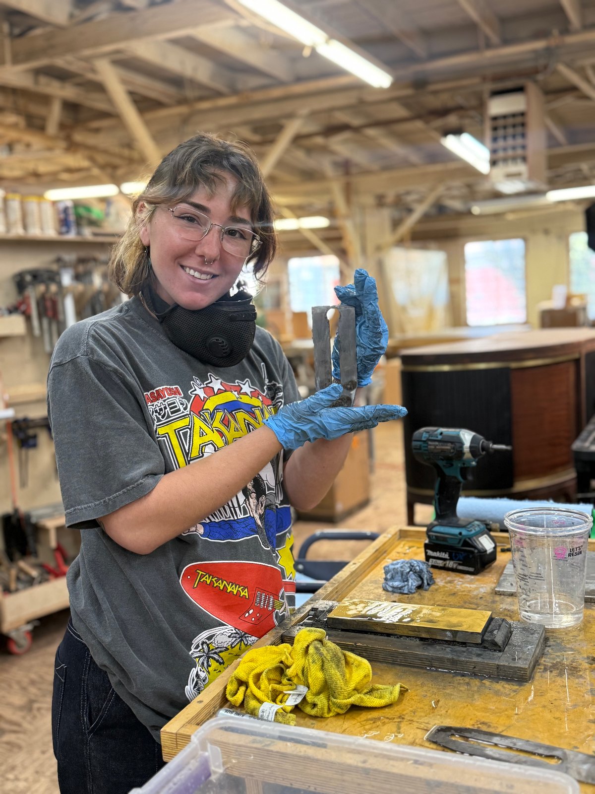 Tressa Digianvittorio at the bench in gloves, holding up two small pieces she has been working on